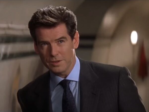 Pierce Brosnan stands smiling in disbelief in Q